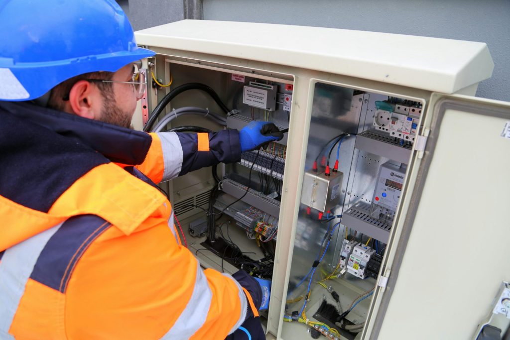 Ingénieur en équipement de sécurité travaillant sur un panneau électrique extérieur, assurant la fonctionnalité du système.