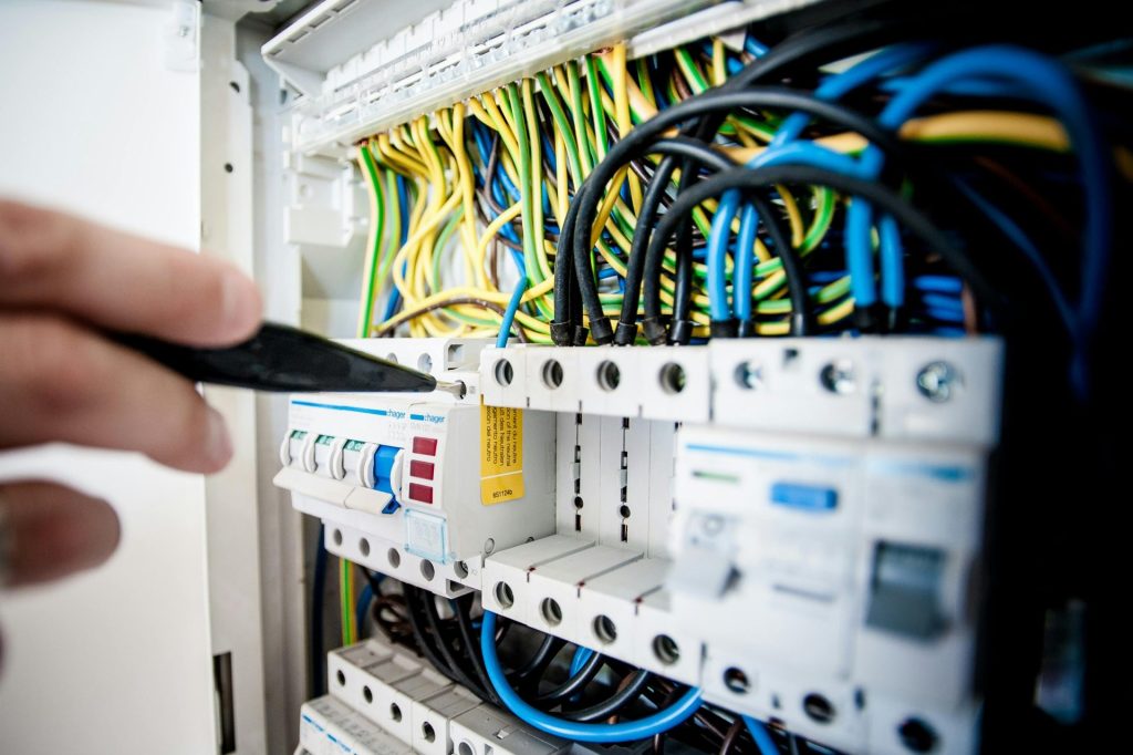 Main d'électricien travaillant sur un panneau de disjoncteurs avec des fils colorés, assurant des connexions électriques sûres.