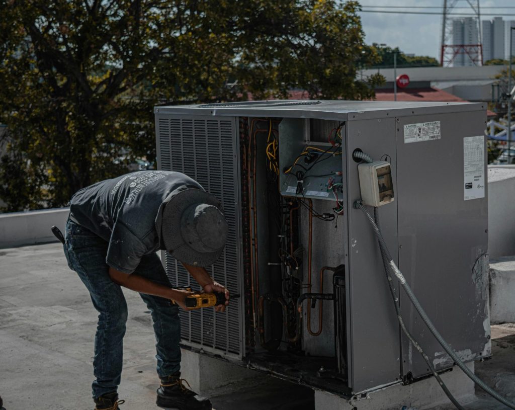 Un technicien répare un climatiseur sur un toit, démontrant ainsi son savoir-faire manuel.