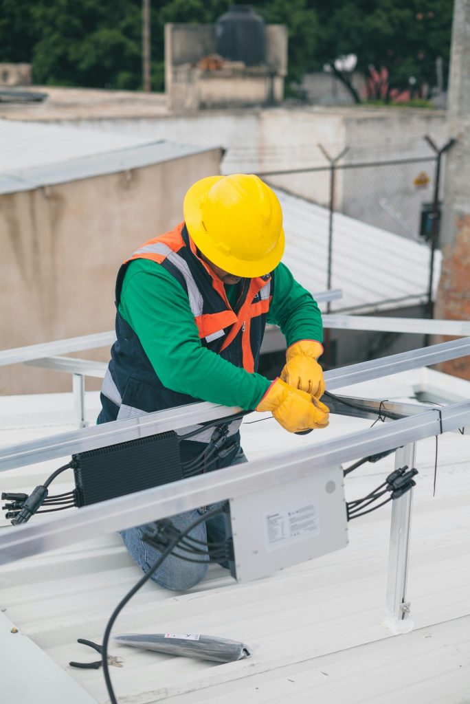 Électricien avec EPI travaillant sur l'installation de panneaux solaires sur le toit, en se concentrant sur la sécurité.